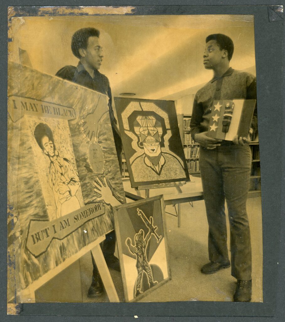 Two men standing near art displays, from the Navarre Branch Library scrapbook